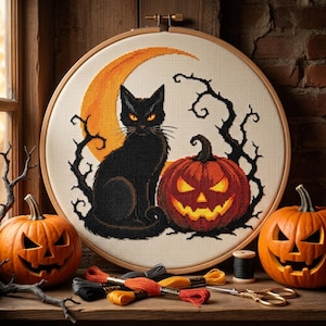 May include: A circular wooden embroidery hoop containing a cross-stitch design of a black cat sitting next to a glowing orange jack-o'-lantern in front of a crescent moon, surrounded by black leafless branches on a cream-colored fabric background.