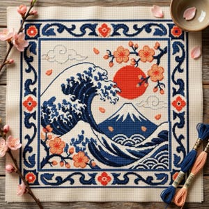 Può includere: Un ricamo a punto croce quadrato su tessuto color crema raffigurante una grande onda oceanica blu scuro, un sole rosso e una cima di montagna. Il disegno è incorniciato da un bordo blu scuro con accenti floreali arancioni e rami di ciliegio.