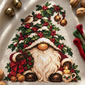 Può includere: Un ricamo a punto croce su tessuto beige raffigurante uno gnomo con una lunga barba bianca, che indossa un cappello decorato con rami di pino verdi, bacche rosse e due campanellini dorati pendenti. Un piccolo uccellino è sul cappello e una candela.