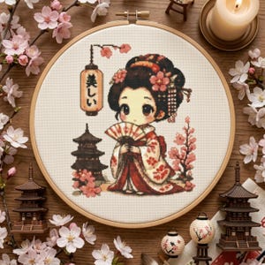 以下が含まれることがあります： 円形の木製刺繍枠に入ったクロスステッチ刺繍。赤と白の着物を着て扇子を持つキャラクターが描かれています。デザインには、暗い色の五重塔、日本語で「美しい」と書かれた吊り下げ式の提灯、そしてピンクの桜の花が含まれています。