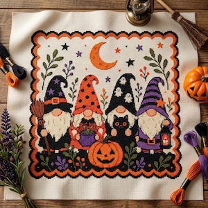 Può includere: Un ricamo a punto croce su tessuto color crema raffigurante quattro gnomi con cappelli da stregone, una luna crescente, stelle e una zucca, racchiusi in un bordo smerlato arancione e nero, circondato da fili da ricamo e una scopa.
