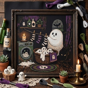 May include: A framed cross-stitch embroidery depicting a ghost hanging striped socks on a clothesline above a laundry basket filled with smaller ghosts. The scene includes a washing machine, a skull rug, and shelves with bottles.