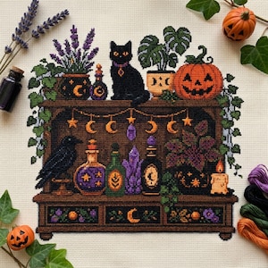 May include: A cross-stitch embroidery on cream fabric depicting a wooden shelf filled with magical items. Features include a black cat, a jack-o'-lantern, potted plants, purple crystals, glass potion bottles, a black raven, and a hanging moon garland.
