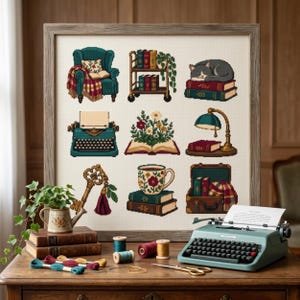 May include: A framed cross-stitch sampler featuring nine distinct illustrations: a teal armchair, a rolling book cart, a cat on books, a teal typewriter, an open book with flowers, a desk lamp, a gold key, a floral mug on books, and a suitcase.