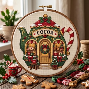 Può includere: Un telaio da ricamo rotondo in legno contenente un motivo a punto croce di un negozio a forma di teiera verde con la parola COCOA stampata sopra. Il design presenta un manico a bastoncino di zucchero, una ghirlanda sulla porta e decorazioni.