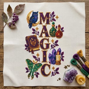 Op de afbeelding: Een kruissteekpatroon op witte stof met het woord MAGIC in paarse en gouden letters. Het ontwerp bevat een blauwe uil op een maansikkel, een paars boek, een groene nachtvlinder, toverdrankflesjes, kristallen en een kaars met bladeren.