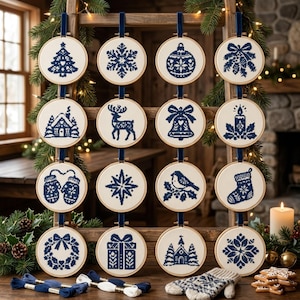 May include: Sixteen circular embroidery hoops featuring navy blue cross-stitch designs on cream fabric. Patterns include a Christmas tree, snowflake, ornament, mistletoe, cabin, reindeer, bell, candle, mittens, star, bird, stocking, wreath, gift, church, and snowflake.