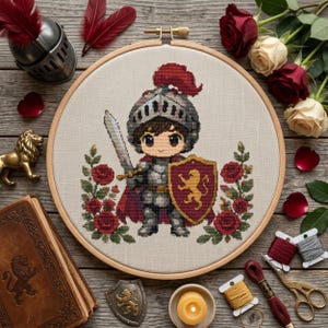 May include: A cross-stitch embroidery in a circular wooden hoop featuring a cartoon knight in silver armor with a red plume, holding a sword and a shield with a gold lion emblem, framed by red roses on a light fabric background.