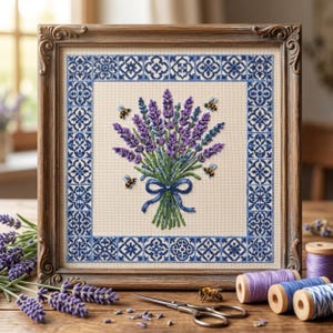 Puede incluir: Un bordado en punto de cruz enmarcado que presenta un ramo central de lavanda morada atado con una cinta azul, rodeado por tres pequeñas abejas. El diseño está encerrado en un borde de patrón geométrico azul y blanco sobre tela crema.