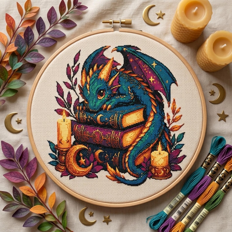 May include: A circular wooden embroidery hoop containing a cross-stitch pattern of a teal and gold dragon resting on a stack of books, surrounded by candles and foliage. The design features vibrant colors, including purple and orange accents.