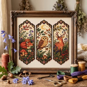 May include: A framed cross-stitch embroidery featuring three vertical panels depicting a sleeping fox, a perched owl under a crescent moon, and a standing deer, all surrounded by detailed forest flora, mushrooms, and foliage in a dark wood frame.