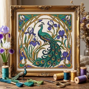 May include: A framed cross-stitch embroidery featuring a peacock surrounded by purple and white iris flowers within an oval border. The artwork is displayed in an ornate gold frame, accompanied by spools of colorful thread and a small peacock figurine.