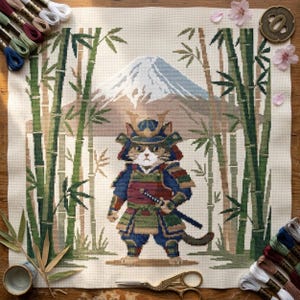 Könnte beinhalten: Ein Kreuzstich-Stickprojekt auf cremefarbenem Stoff, das eine Katze in einer blau-grünen Samurai-Rüstung mit einem Katana zeigt. Der Hintergrund zeigt einen Berg mit schneebedecktem Gipfel, umrahmt von grünen Bambusstangen und rosa Blütenblättern.