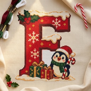 May include: A cross-stitch pattern of the letter E in red with white snowflakes, topped with snow, holly, and berries. A penguin wearing a Santa hat and green scarf stands next to two wrapped gifts and a candy cane on cream fabric.