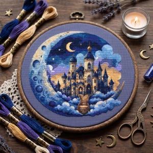 May include: A circular wooden embroidery hoop containing a cross-stitch design of a castle nestled within a crescent moon and clouds. The scene features shades of blue, purple, and gold, accompanied by embroidery floss, scissors, and charms.