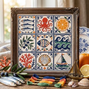 May include: A framed cross-stitch sampler featuring a grid of nine square tiles with Mediterranean-inspired motifs including sardines, an octopus, an orange slice, olives, a patterned fish, ocean waves, coral, a seashell, and a sailboat.