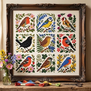 Op de afbeelding: Een ingelijst kruissteekborduurwerk met een raster van negen verschillende vogels, elk omringd door botanische elementen zoals bloemen en bladeren. Het kunstwerk zit in een donkere, sierlijke houten lijst, vergezeld van gekleurd borduurgaren.
