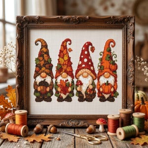 May include: A framed cross-stitch embroidery featuring four gnomes with tall hats decorated with autumn leaves, mushrooms, and pumpkins. The gnomes have white beards and are arranged in a row. The piece is displayed in a dark brown ornate frame.