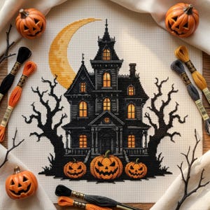 May include: A cross-stitch pattern on cream fabric featuring a black haunted house with glowing yellow windows, a large yellow crescent moon, and three jack-o'-lanterns. The design is surrounded by black bare trees and embroidery floss.