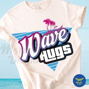 Może przedstawiać: Kremowa koszulka z napisem "Wave Hugs" w stylu retro, w kolorach niebieskim i różowym. Projekt zawiera niebieski trójkąt, palmy i wzór retro fali.