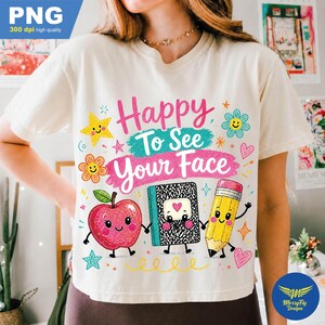 May include: A cream-colored t-shirt featuring a colorful graphic with the text "Happy To See Your Face." The design includes a smiling red apple, a black and white speckled composition notebook, and a yellow pencil, all with arms and legs.