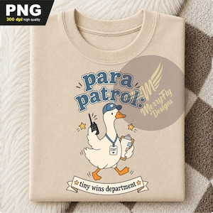 May include: A beige t-shirt featuring a graphic of a white goose wearing a blue cap and a staff lanyard. The goose holds a walkie-talkie and a clipboard. The text reads "para patrol" and "tiny wins department" with yellow star accents.