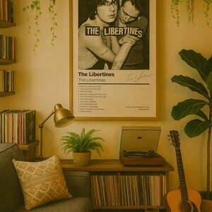 Könnte beinhalten: Gemütliches Wohnzimmer mit einem gerahmten Poster der Band The Libertines. Der Raum verfügt über ein graues Sofa, einen Holz-Plattenspieler, eine Gitarre und einen kleinen runden Tisch. Pflanzen und eine Lampe sorgen für eine warme Atmosphäre.