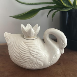 Peut inclure: Figurine de cygne en céramique crème avec un couvercle en forme de fleur de lotus. Le cygne présente des textures de plumes détaillées et un cou incurvé. Objet décoratif pour la maison ou le bureau.