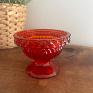 May include: A vibrant red glass pedestal bowl with a diamond-cut pattern. The bowl has a round base and a wide, shallow top, suitable for displaying small items. The bowl is approx. 10 cm in diameter and 7.6 cm tall.