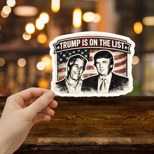 May include: A sticker with the text "TRUMP IS ON THE LIST" above an image of two men in front of an American flag. The sticker has a distressed, vintage look.
