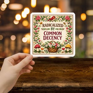 May include: A square sticker with a floral design and the text "RADICALIZED BY COMMON DECENCY." The sticker features a red bird, mushrooms, a basket of flowers, and a bee. The border is a cream color.