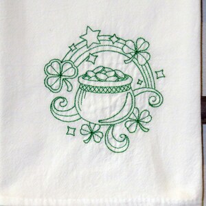 May include: White towel with a green embroidered design featuring a pot of gold, shamrocks, a rainbow, and stars. The design is centered on the towel, creating a festive St. Patrick's Day theme.