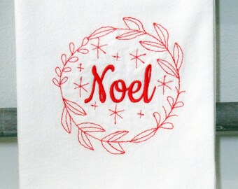 Puede incluir: Toalla de cocina blanca con texto bordado en rojo que dice "Noel" dentro de una corona de hojas y copos de nieve. La toalla está hecha de un material suave y absorbente, ideal para la temporada navideña.