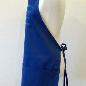 May include: A blue apron with a white embroidered saying "Happiness is homemade" on the front. The apron has a large pocket and ties at the waist.