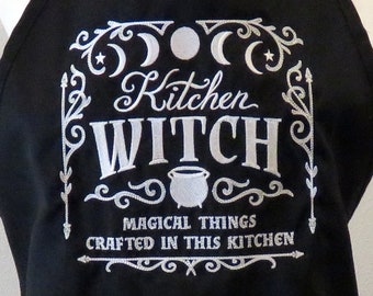 May include: Black kitchen apron with white embroidery that reads "Kitchen Witch" with a crescent moon and star design. The text "Magical things crafted in this kitchen" is also embroidered on the apron.