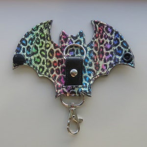 May include: A rainbow glitter bat-shaped keychain with a black leather strap and a silver swivel clip.