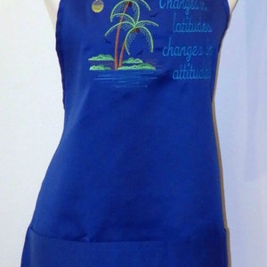 May include: A blue apron with a pocket and adjustable straps. It features an embroidered design of palm trees and the text "Changes in latitude changes in attitude."