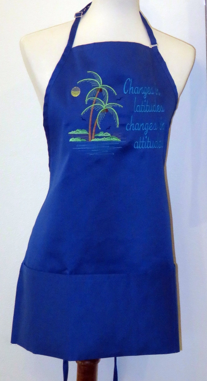 May include: A blue apron with a pocket and adjustable straps. It features an embroidered design of palm trees and the text "Changes in latitude changes in attitude."