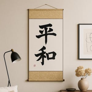 Puede incluir: Un pergamino con caligrafía japonesa, con los caracteres de "paz" en tinta negra. El pergamino está enmarcado por un borde beige y clavijas de madera. La obra de arte cuelga en un salón de tonos neutros.