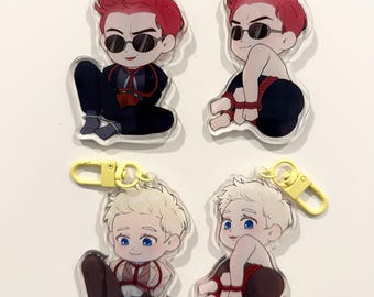 May include: Four clear acrylic keychains featuring cartoon illustrations of two characters. One character has red hair and sunglasses, the other has blonde hair and blue eyes. Each keychain has a yellow clasp and a brown leather strap.