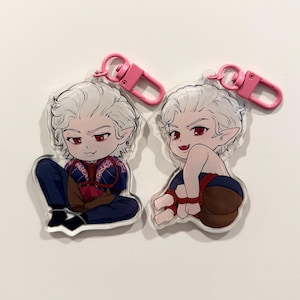May include: Two acrylic keychains featuring a cartoon character with white hair, red eyes, and pointed ears. One keychain shows the character in a blue and red outfit, the other is partially nude. Both have pink clasps.
