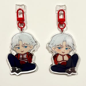 May include: Two clear acrylic keychains featuring a chibi-style character with white hair, blue eyes, and a red jacket. The character is seated with legs crossed, wearing dark blue pants. Each keychain has a red clasp.