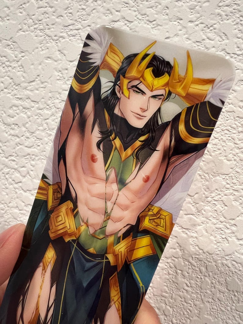 May include: A rectangular bookmark featuring a stylized illustration of a character with long black hair, a golden crown, and a green and gold outfit. The character is depicted with their arms raised.