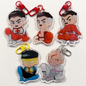May include: A collection of five cartoon character keychains. Each keychain features a different character design with a red or yellow clasp. The characters are depicted in various poses and outfits, with a clear acrylic backing.