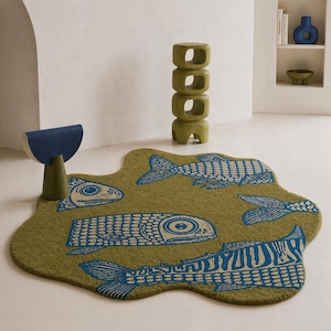 Könnte beinhalten: Ein olivgrüner Teppich mit organischem Design, verziert mit blauen und beigen Fischmustern. Der Teppich liegt auf einem hellen Boden, neben einem grünen Beistelltisch und einem blau-beigen Akzenttisch. Ungefähre Größe: 180 cm x 120 cm.