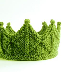 Könnte beinhalten: Eine gestrickte grüne Krone mit einem strukturierten Blättermuster. Die Krone hat eine Reihe von spitzen Spitzen, die jeweils mit einem kleinen, abgerundeten Detail versehen sind. Das Garn ist ein leuchtender Grünton.