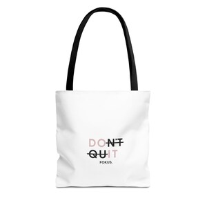 May include: White tote bag with black handles featuring the text "DON'T QUIT" in a pink and black font, with the word "QUIT" crossed out. The word "FOKUS" is below the text.