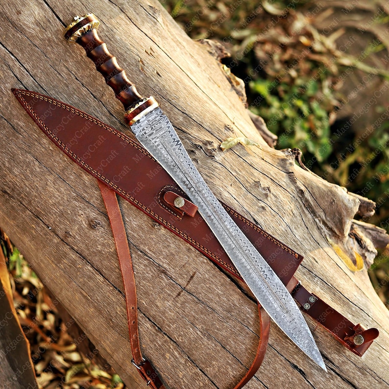 May include: A detailed image of a sword with a patterned blade and a wooden handle. The sword is sheathed in a brown leather scabbard with a strap. The blade has a decorative design.