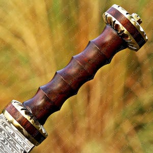 May include: Close-up of a sword hilt with a dark wooden handle and brass accents. The handle has a ridged design for grip. The pommel and guard feature intricate metalwork and a contrasting wood grain.