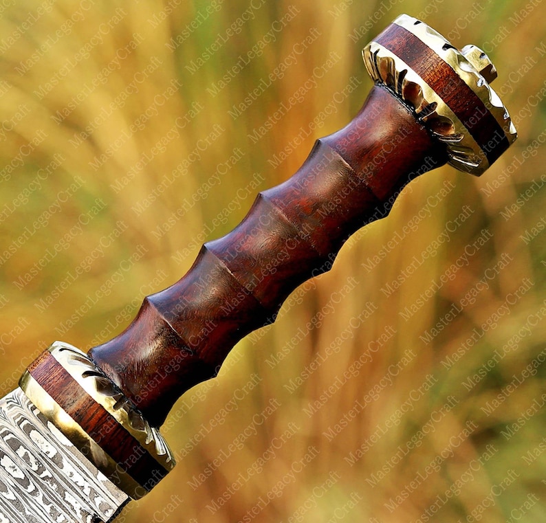 May include: Close-up of a sword hilt with a dark wooden handle and brass accents. The handle has a ridged design for grip. The pommel and guard feature intricate metalwork and a contrasting wood grain.